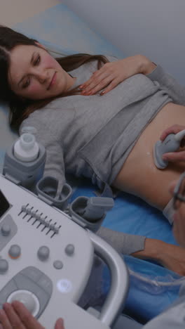 Female-doctor-conducts-medical-examination-of-stomach-to-female-patient-using-sonography-machine-with-digital-monitor.-Caucasian-woman-undergoes-ultrasound-diagnostics-in-modern-clinic-or-hospital.